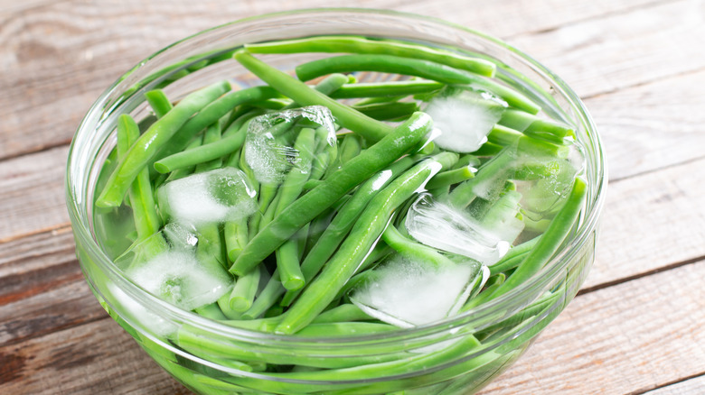 Ice cubes rest with green beans in a bowl.