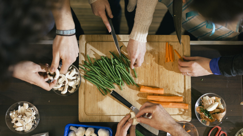People's hands are working on ingredients, including cutting green beans and carrots.