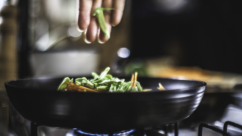 A hand is seen putting green beans in a pan.
