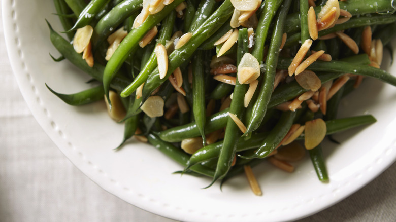 Green beans with almonds sit on a white plate.