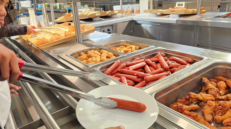 Someone putting sausage on their plate at an IKEA food court.