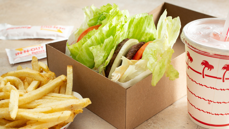 In-N-Out lettuce-wrapped burgers in cardboard box with fries, drink, and packets on beige background