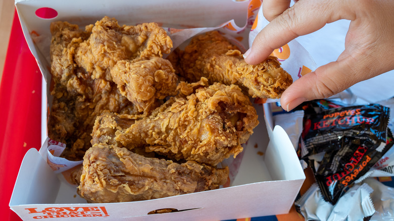 Person grabbing chicken from Popeyes box