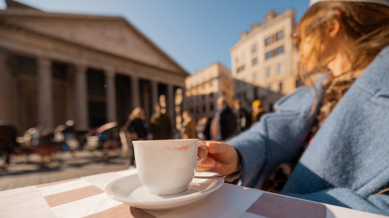 Person holding coffee cup in front of Pantheon in Italy.