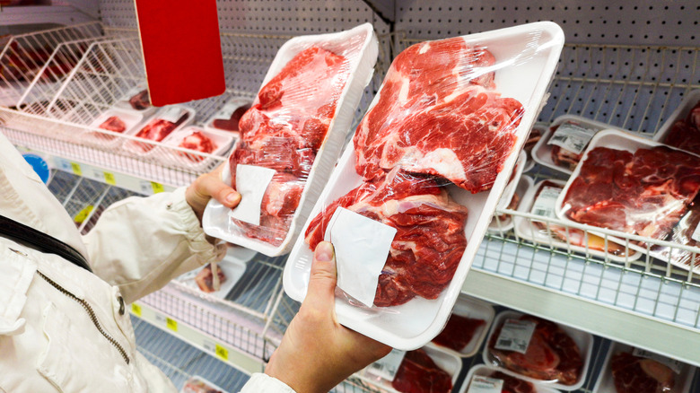 Person comparing packages of meat inside grocery store