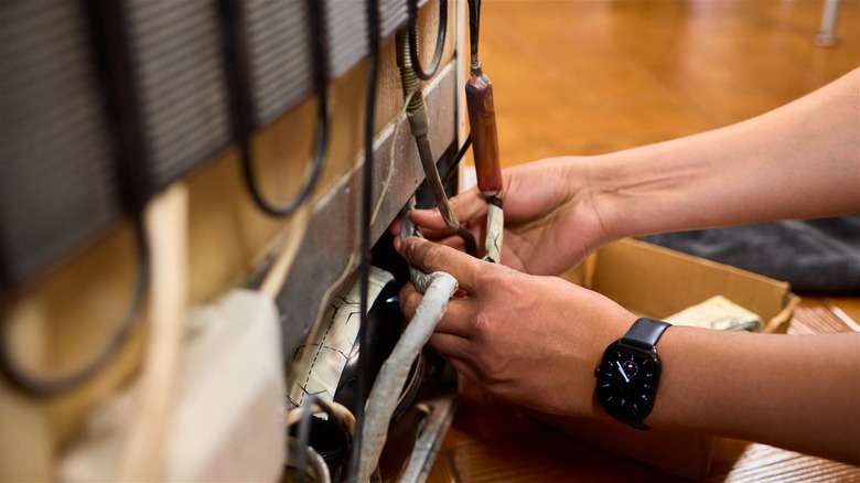 A technician's hands adjusting wiring on the back of a refrigerator.