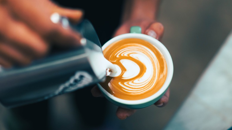 A barista pouring evaporated milk in a coffee cup 