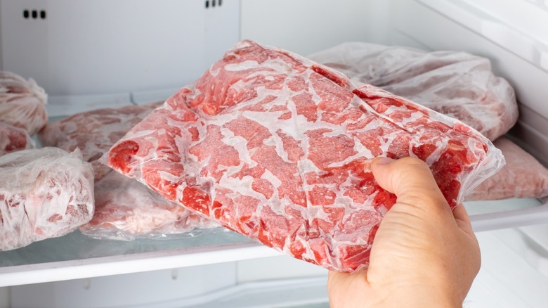 Hand removing frozen meat from freezer with other frozen meats in the background