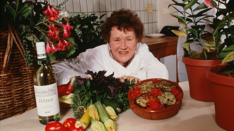 Julia Child smiling in front of vegetables and casserole