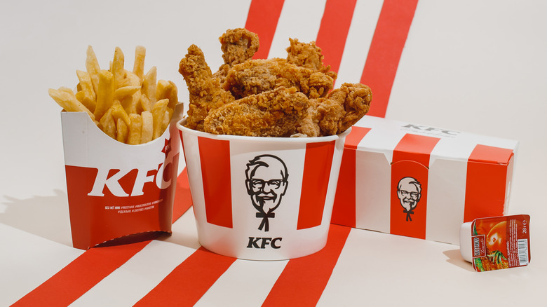 A bucket of fried chicken with Colonel Sanders logo and fries