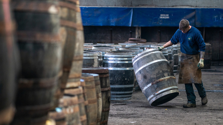 Man inspecting whiskey barrel in warehouse.