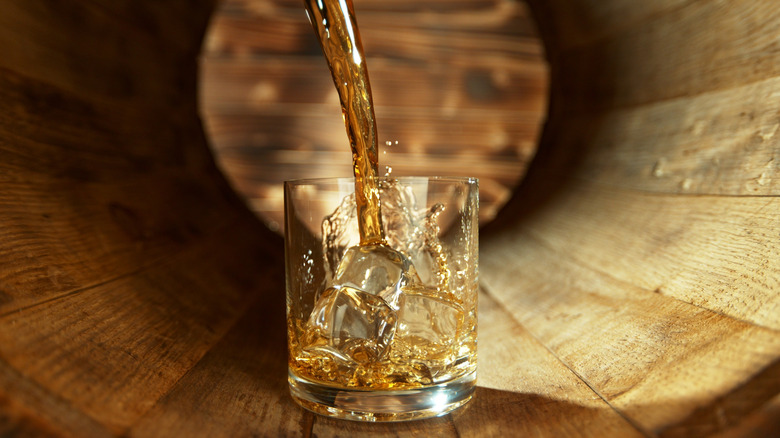 Pouring whiskey into rocks glass inside barrel.