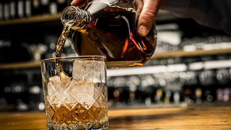 Low angle shot of someone pouring a glass of whiskey into a tumbler.