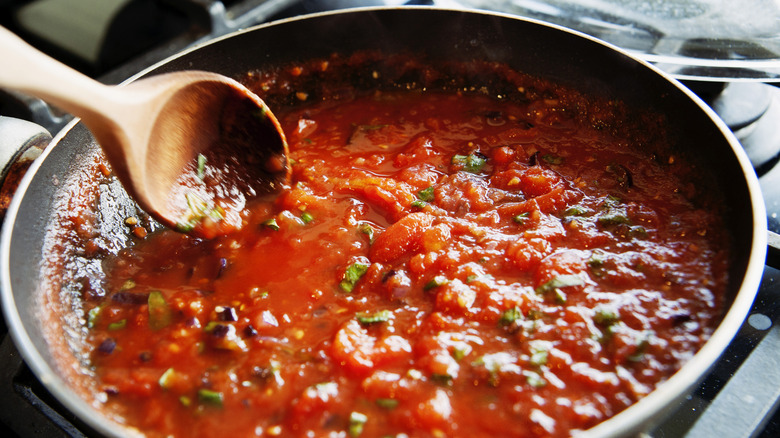 Home cook stirring marinara sauce in a pan on the stove