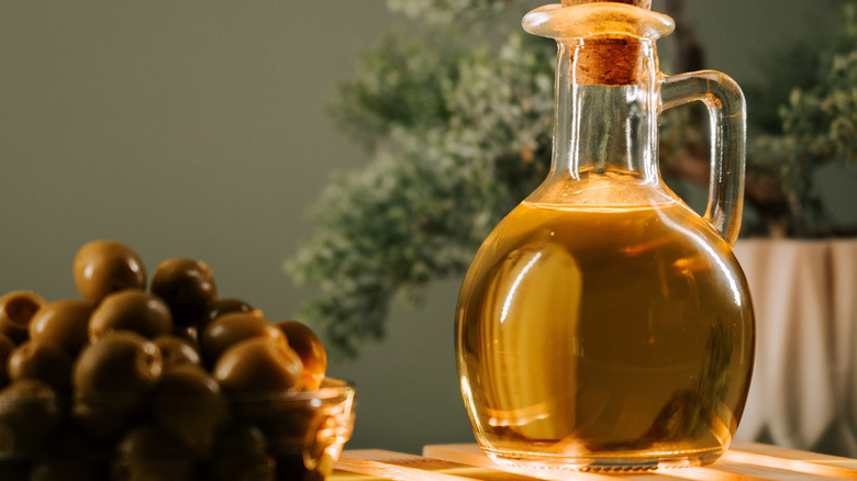 Olive oil in glass bottle next to bowl of olives