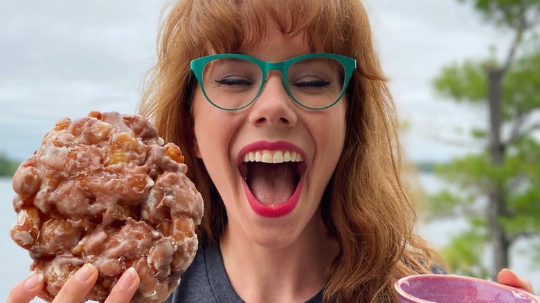 Mary Berg holding fritter and mug of coffee