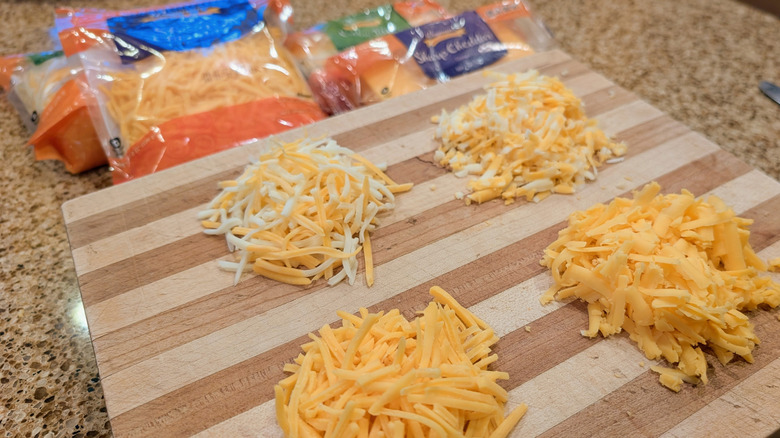Small piles of shredded cheese on a cutting board with packages of cheese visible in the background