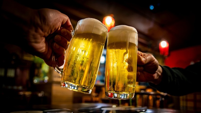 People clinking pints of beer in dark pub