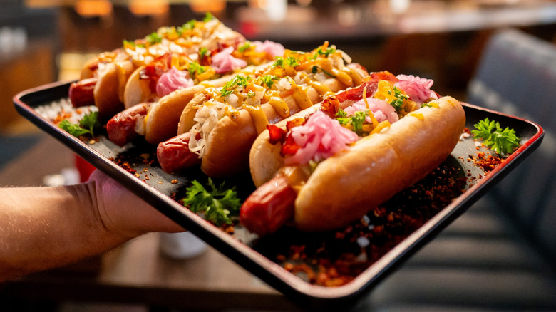 Hand holding tray with four gourmet hot dogs