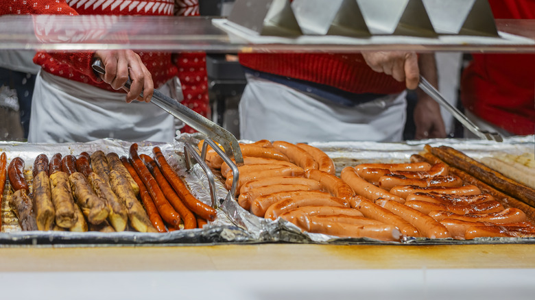 Chefs using tongs to turn sausages on cooking surface