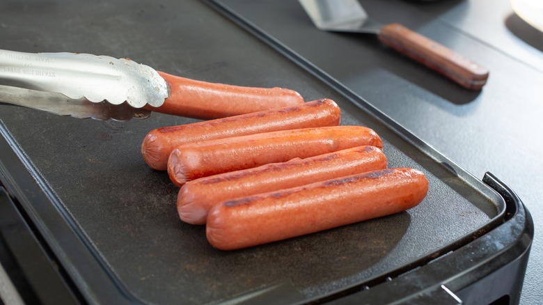 Tongs arranging hot dogs on small griddle