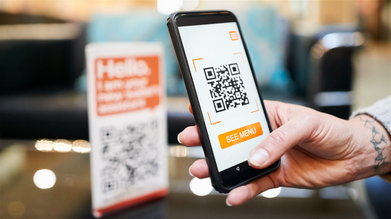 hand holding phone with QR code & "see menu"