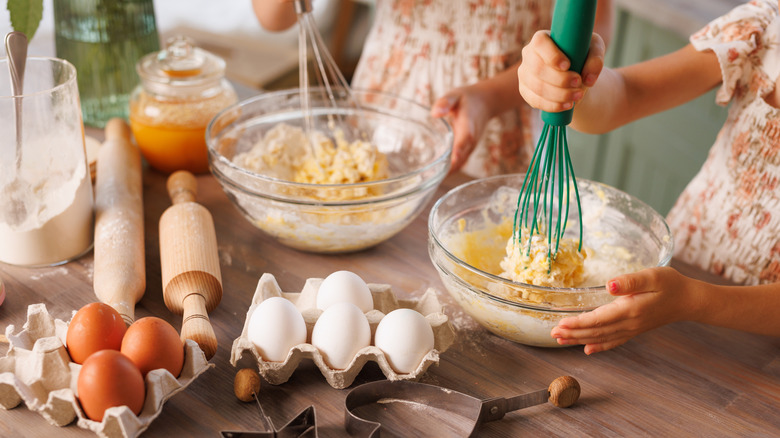 Children whisking dough with baking ingredients on counter.