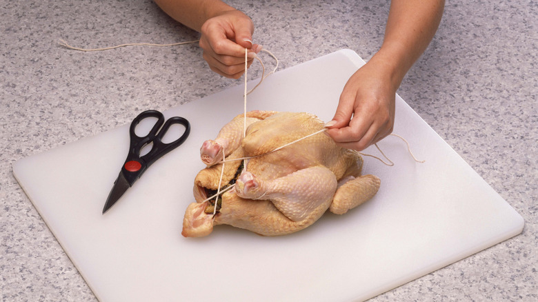 Hands trussing whole chicken with string