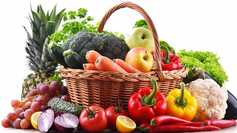 Wicker basket full of broccoli, carrots, apples, peppers, and other fruits and vegetables against white background