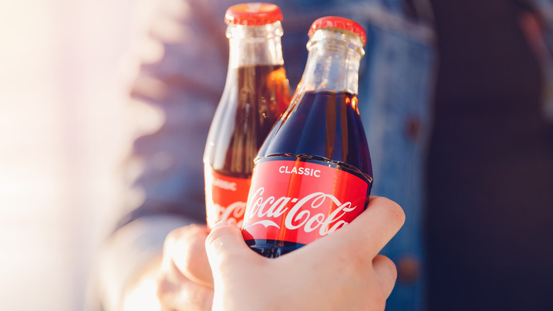 Two people clinking Coca-Cola bottles