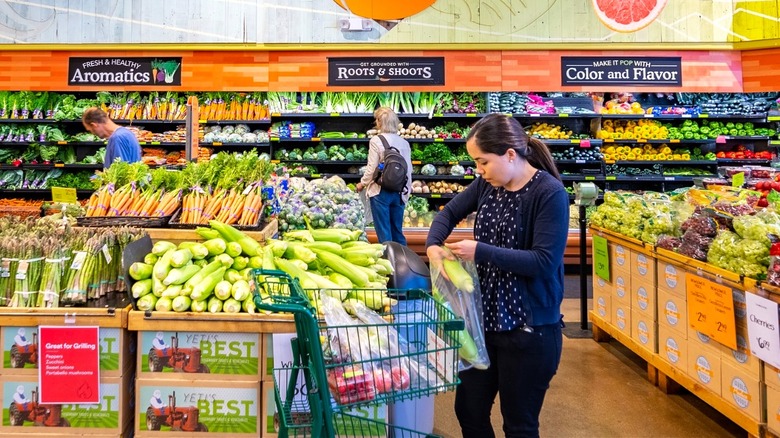 Whole Foods produce section, woman putting corn in bag