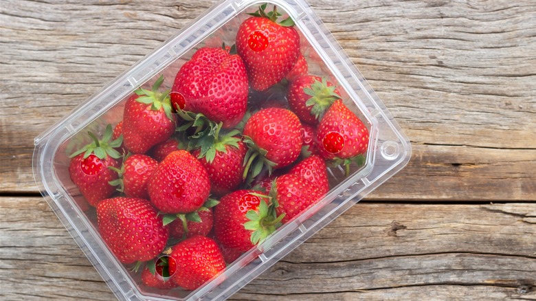 A pack of strawberries on a wooden board