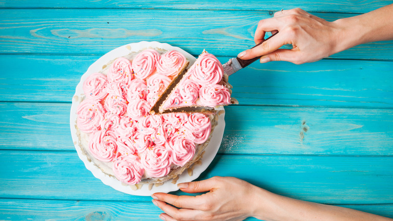 Hand cutting slice of cake with swirls of pink frosting