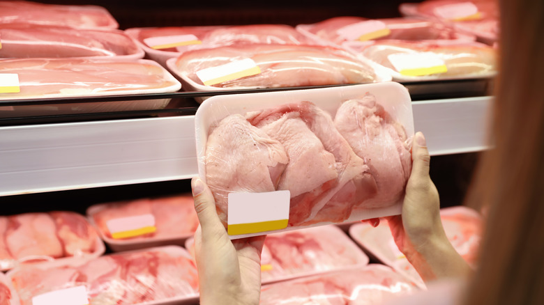 Person holding package of raw chicken at grocery store