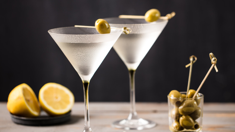 Two martini glasses garnished with olives, with lemons and more olives in the background