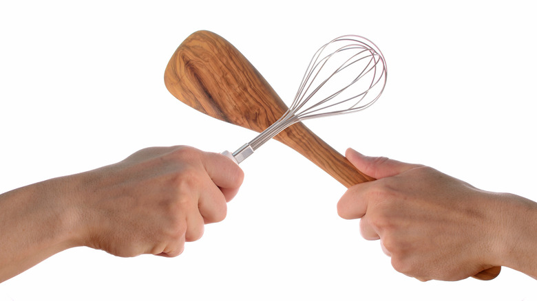 Two people's hands fighting with kitchen utensils