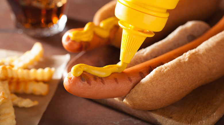 Yellow mustard being squeezed onto a long hot dog