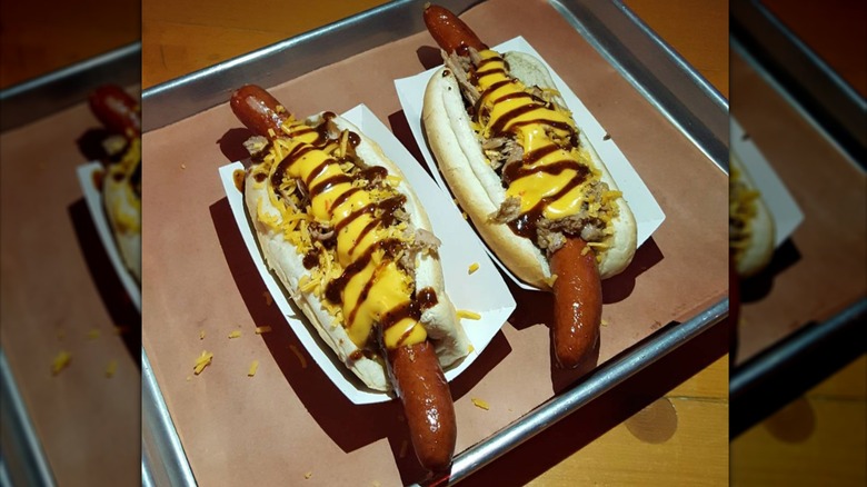Two long hot dogs with various toppings on a metal tray.