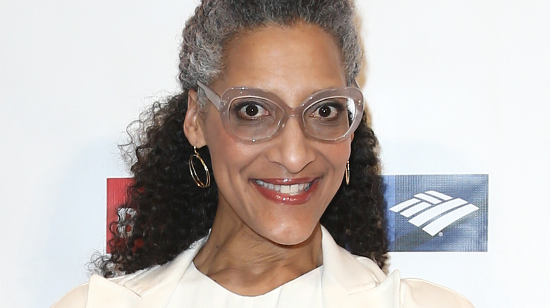 Carla Hall smiles with large-framed glasses