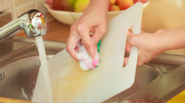 person washing plastic cutting board in sink