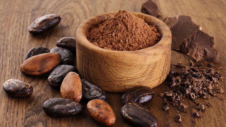 Cocoa beans, powder, crushed cocoa beans and chocolate on wooden background.
