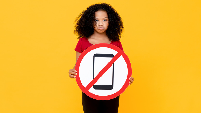 Girl holding no phone sign against yellow backdrop