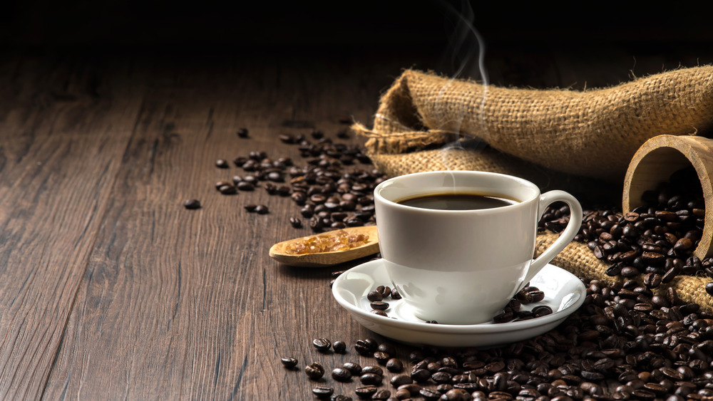 Hot cup of coffee with coffee beans on dark table