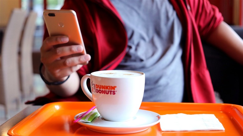 Person on phone sitting with Dunkin' coffee in mug
