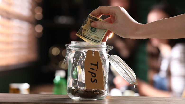 Person dropping $20 into glass tip jar