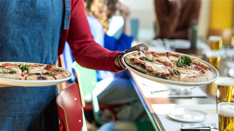 waitress delivering two pizza pies to a table