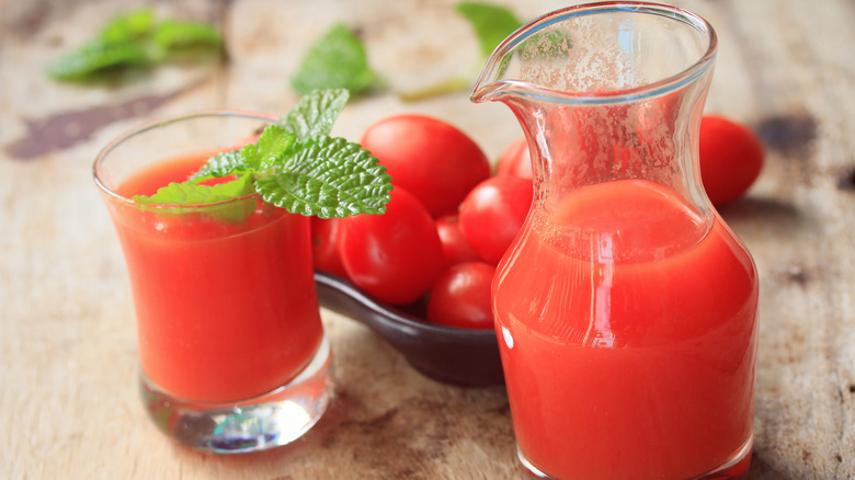 Tomato juice in small jar and herb-garnished glass next to whole cherry tomatoes