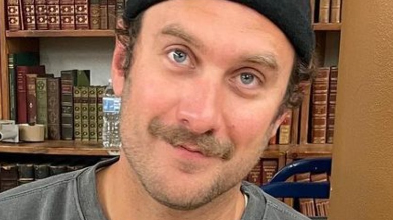 Brad Leone smirking in front of bookshelf while wearing beanie