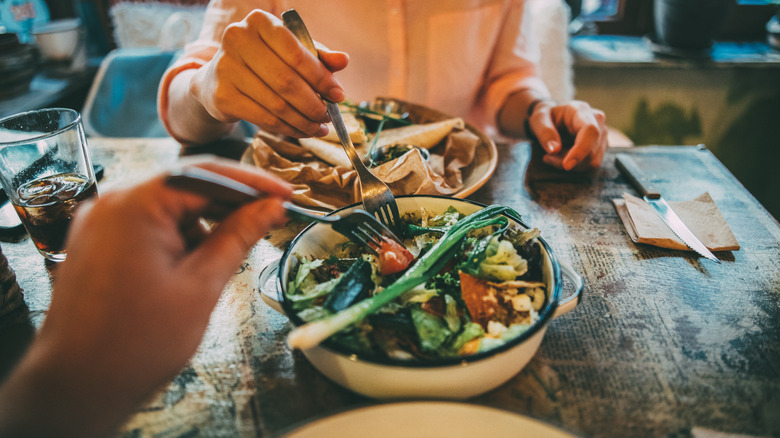 people eating a vegetable dish with forks at a restaurant