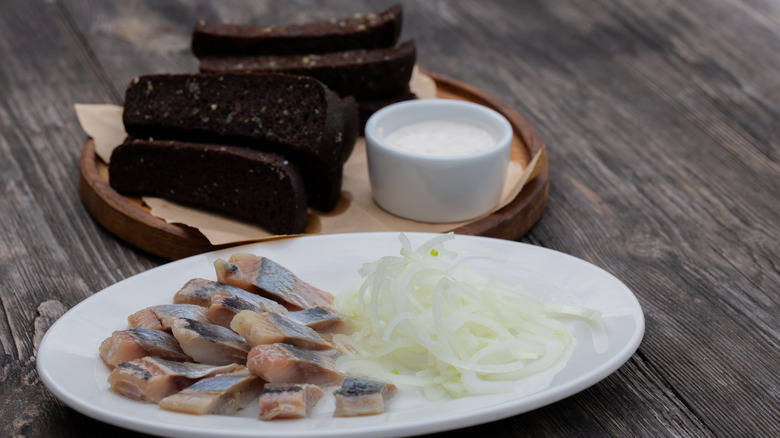 Plate with herring and onion, dark sliced bread in background